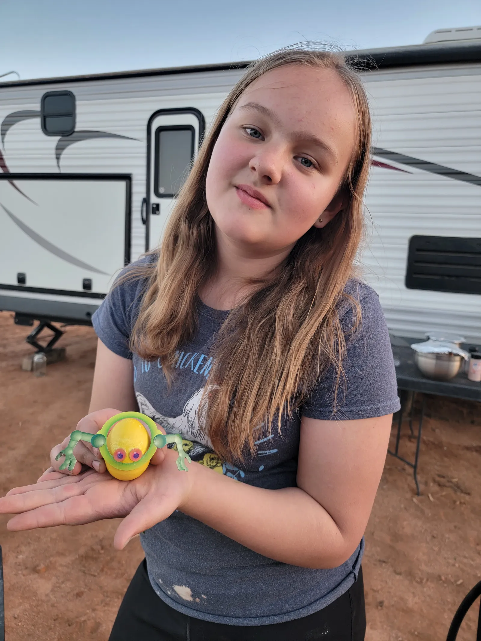 Girl holding a yellow decorated egg with green arms in front of a camper