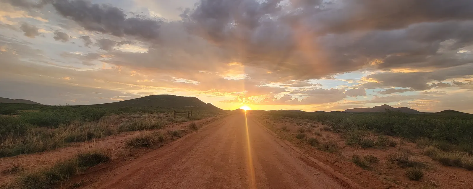 Dirt road running toward a setting sun under dramatic clouds in southern Arizona