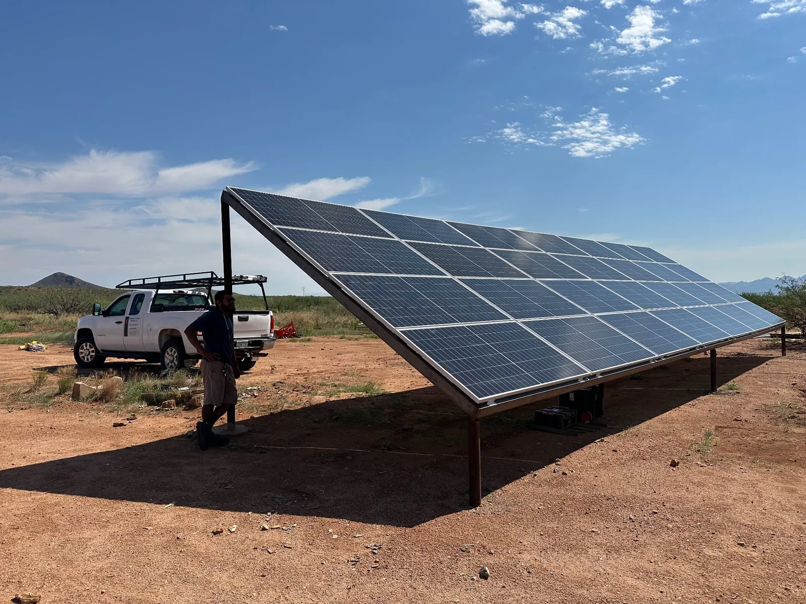 Large ground-mounted solar panel array on our land near Tombstone, Arizona, with a man standing in its shadow beside a white truck